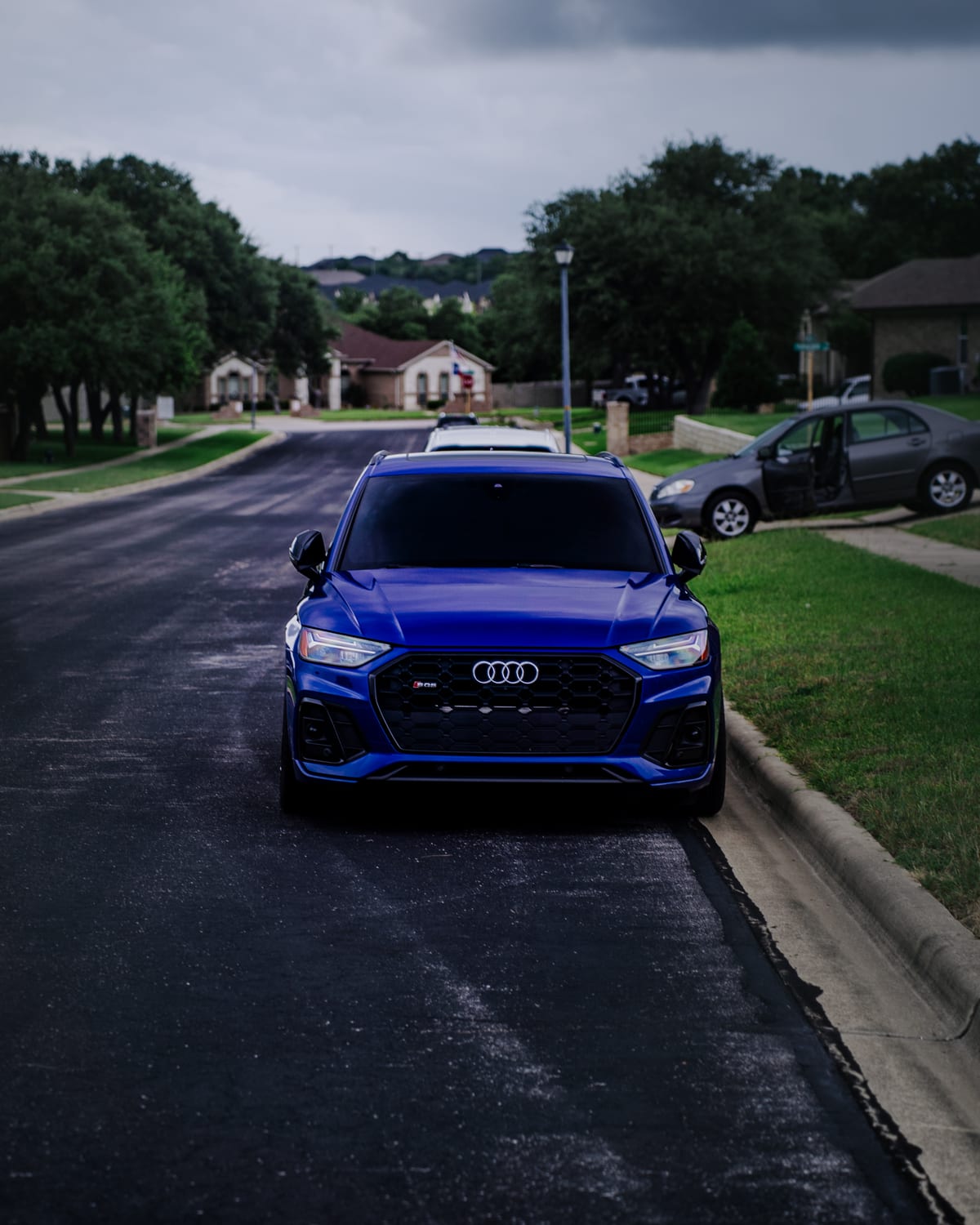 Blue Audi SUV parked on a residential street under a cloudy sky