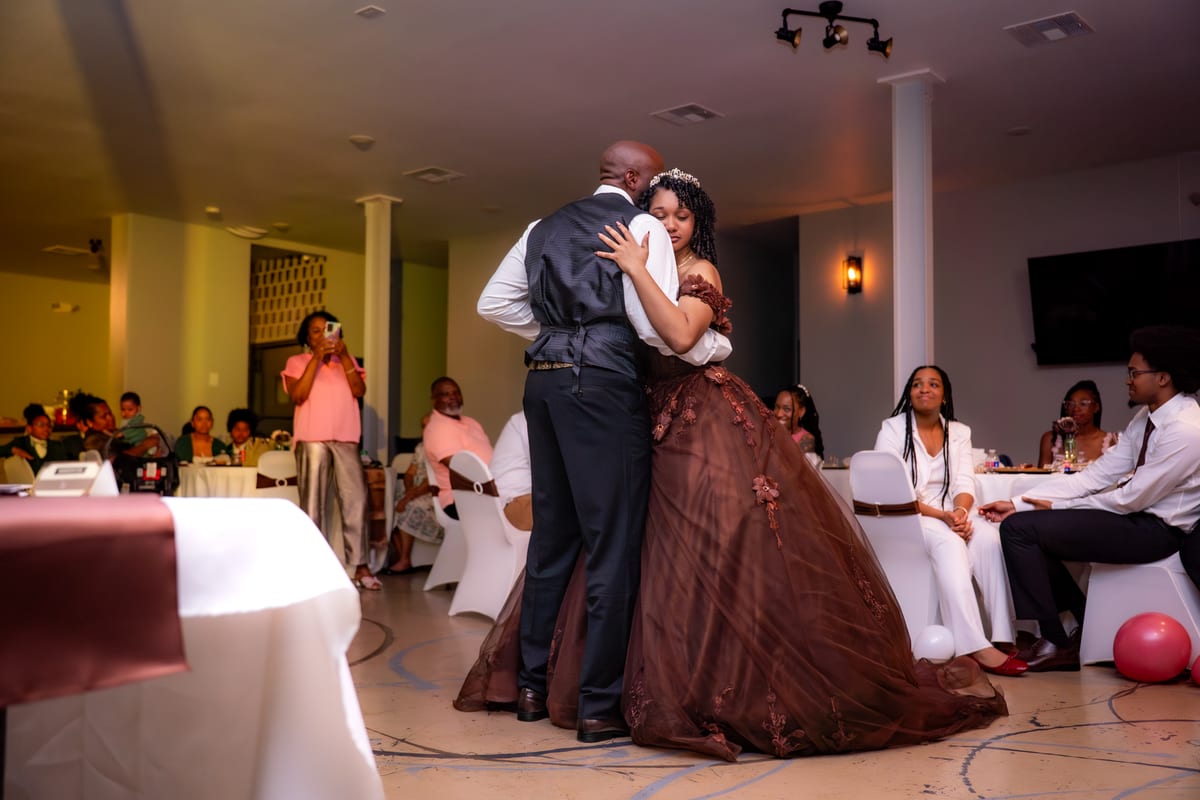 Guest of honor in a tiara and ball gown sharing a slow dance while guests watch from their tables