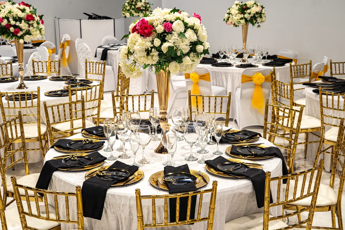 Reception tables set with gold chairs, black napkins, and white floral centerpieces