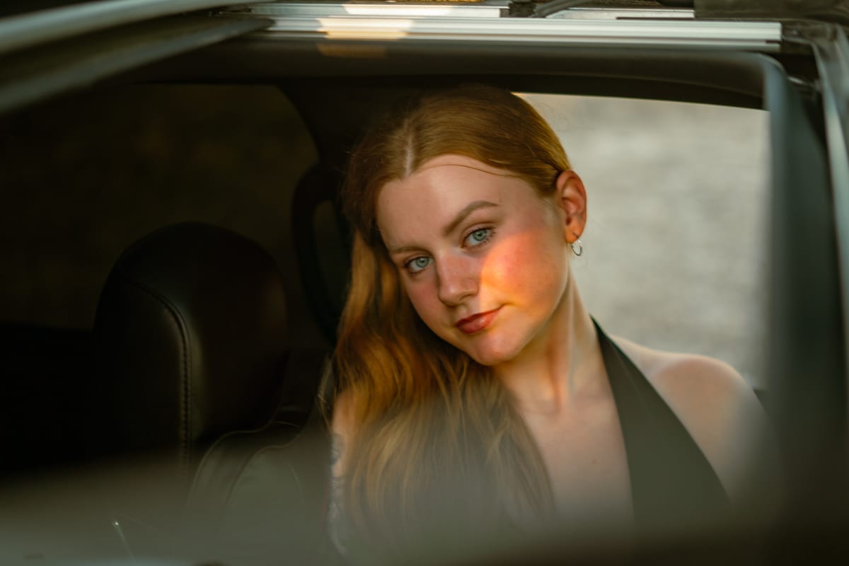 Red-haired woman resting her head on a truck window frame, framed by the dark cab