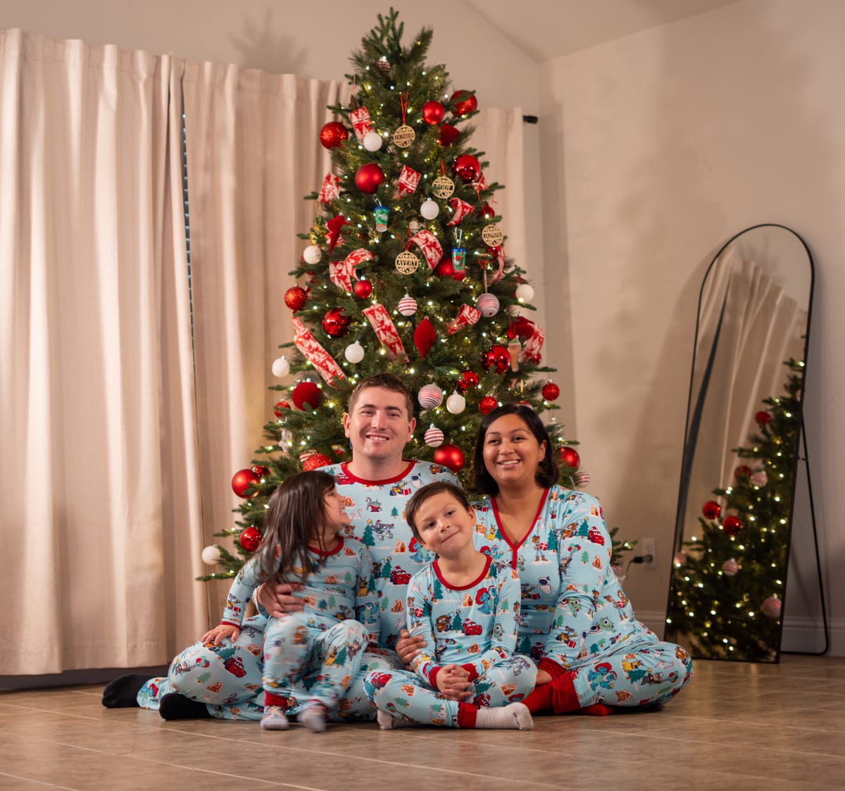 Family of four in matching holiday pajamas sitting in front of a Christmas tree