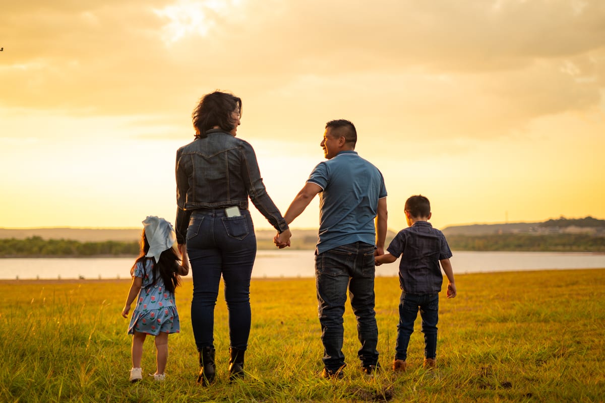 Family of four walking hand in hand toward a lake at golden hour