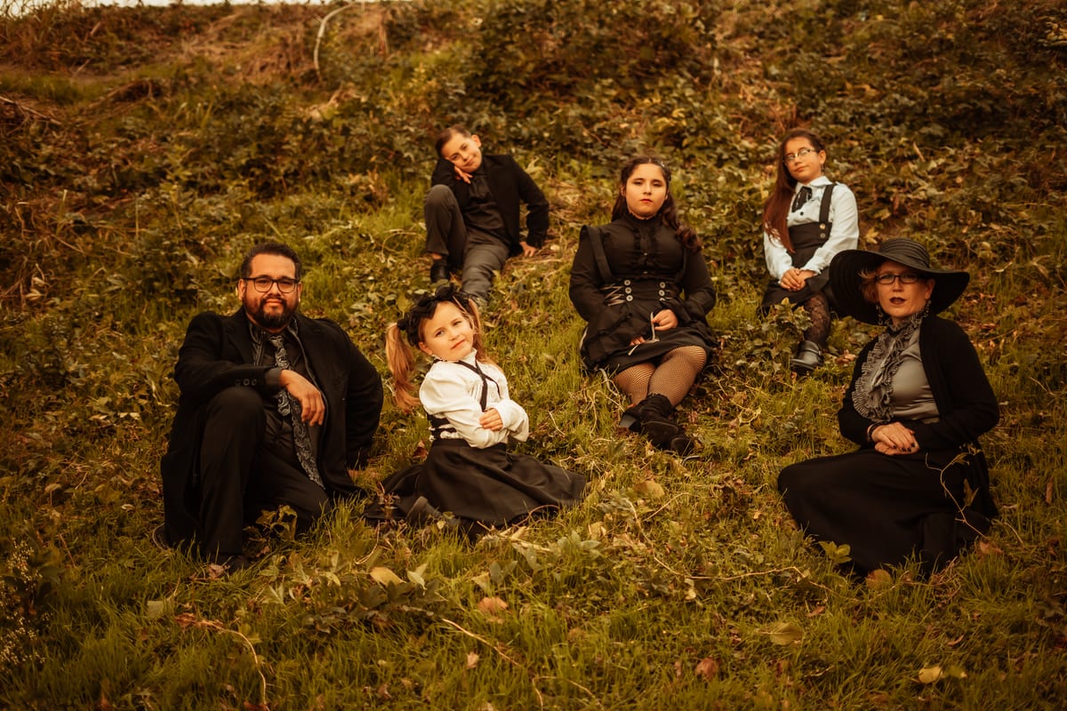 Family in black gothic outfits lying in the grass on a hillside