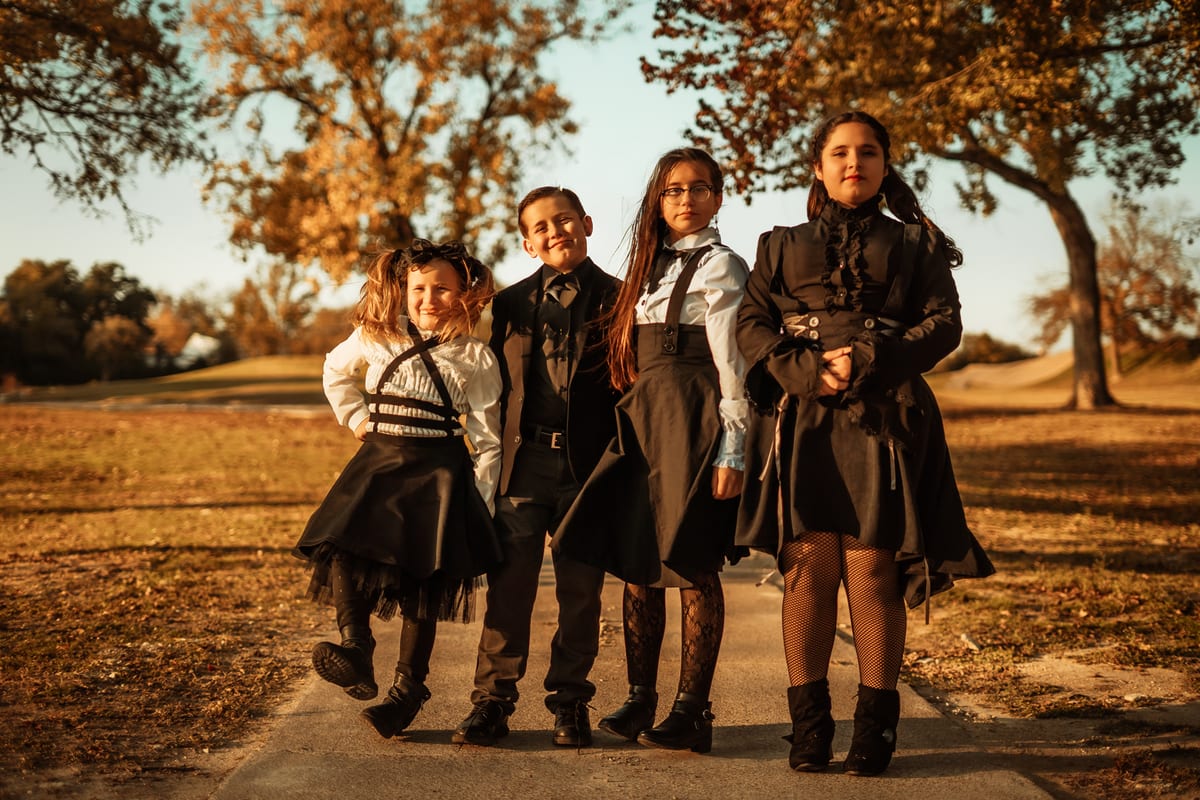 Family in black gothic outfits walking down a park path under autumn trees