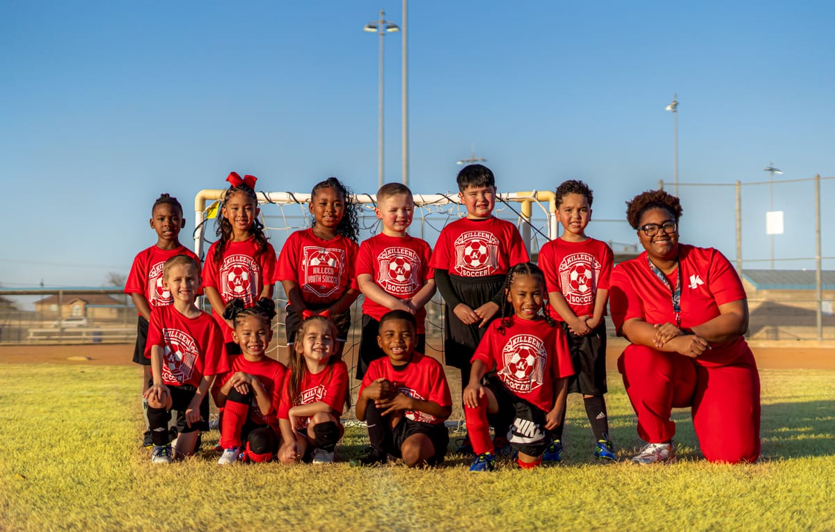 Youth soccer team in red jerseys posed with their coach in front of the goal